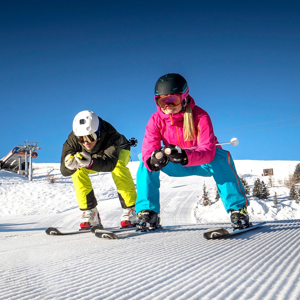 Ein Pärchen fährt gemeinsam eine Skipiste hinunter.