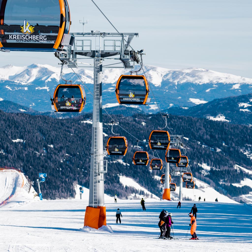 Skiläufer auf einem Seilband im winterlichen Gebirge, umgeben von schneebedeckten Bergen und Wäldern.