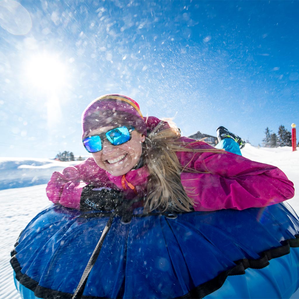 Glückliche Frau auf einem Luftkissen, während sie einen schneebedeckten Berg hinunterrutscht.